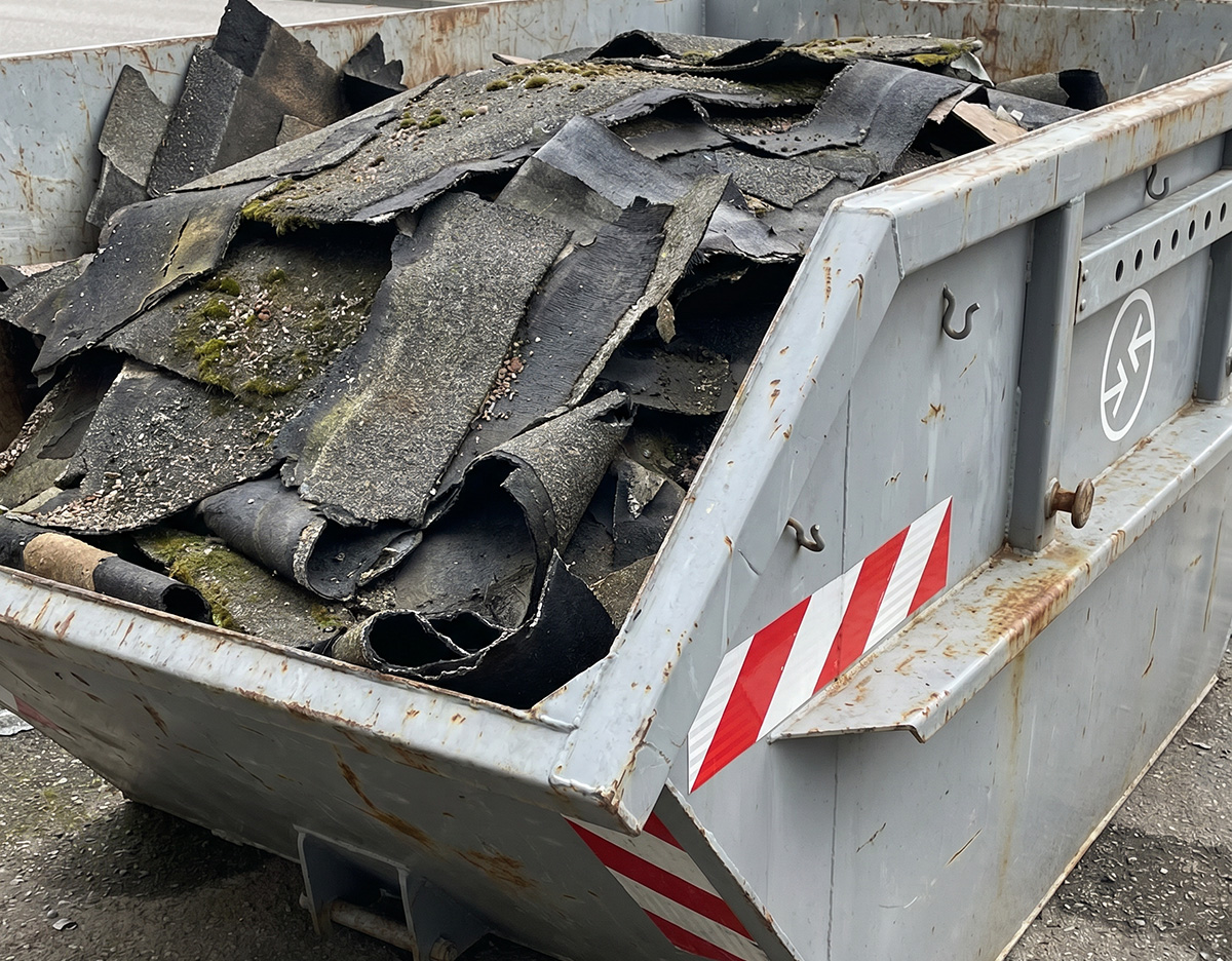 Offener Container gefüllt mit alten, teils moosbewachsenen Dachbahnen auf einem Industriehof.
