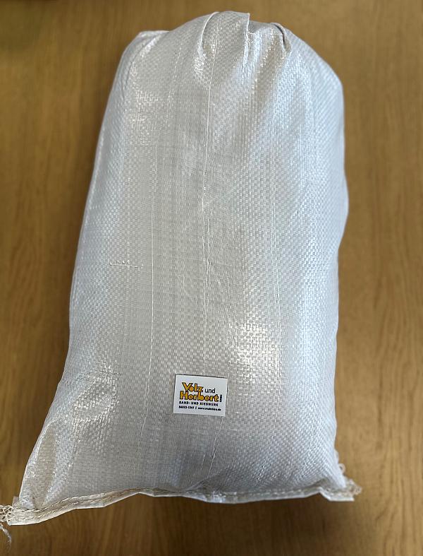 Beiger Kunststoffsack mit Volz und Herbert GmbH Etikett, gefüllt mit Basaltsand, auf Holzboden.