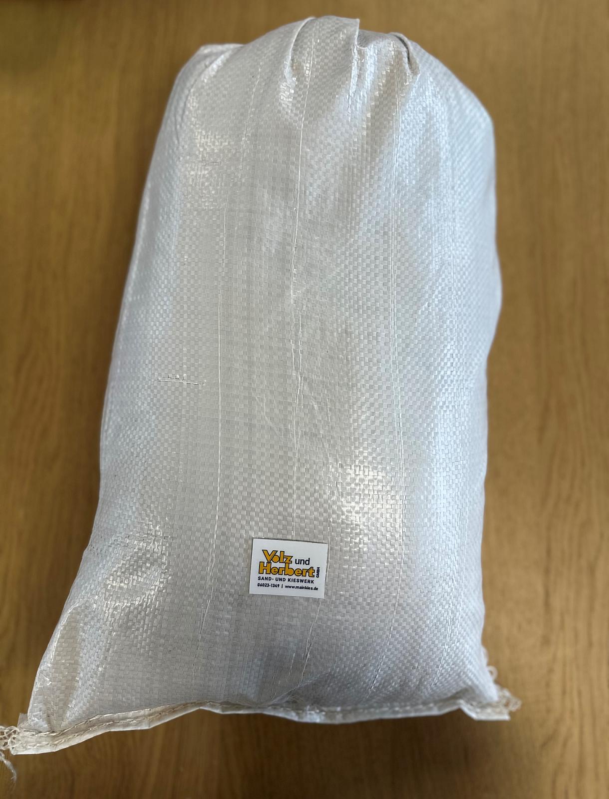 Beiger Kunststoffsack mit Volz und Herbert GmbH Etikett, gefüllt mit Basaltsand, auf Holzboden.