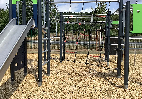Spielplatz mit Klettergerüst und Rutsche auf Bodenbelag aus Hackschnitzeln für Fallschutz.