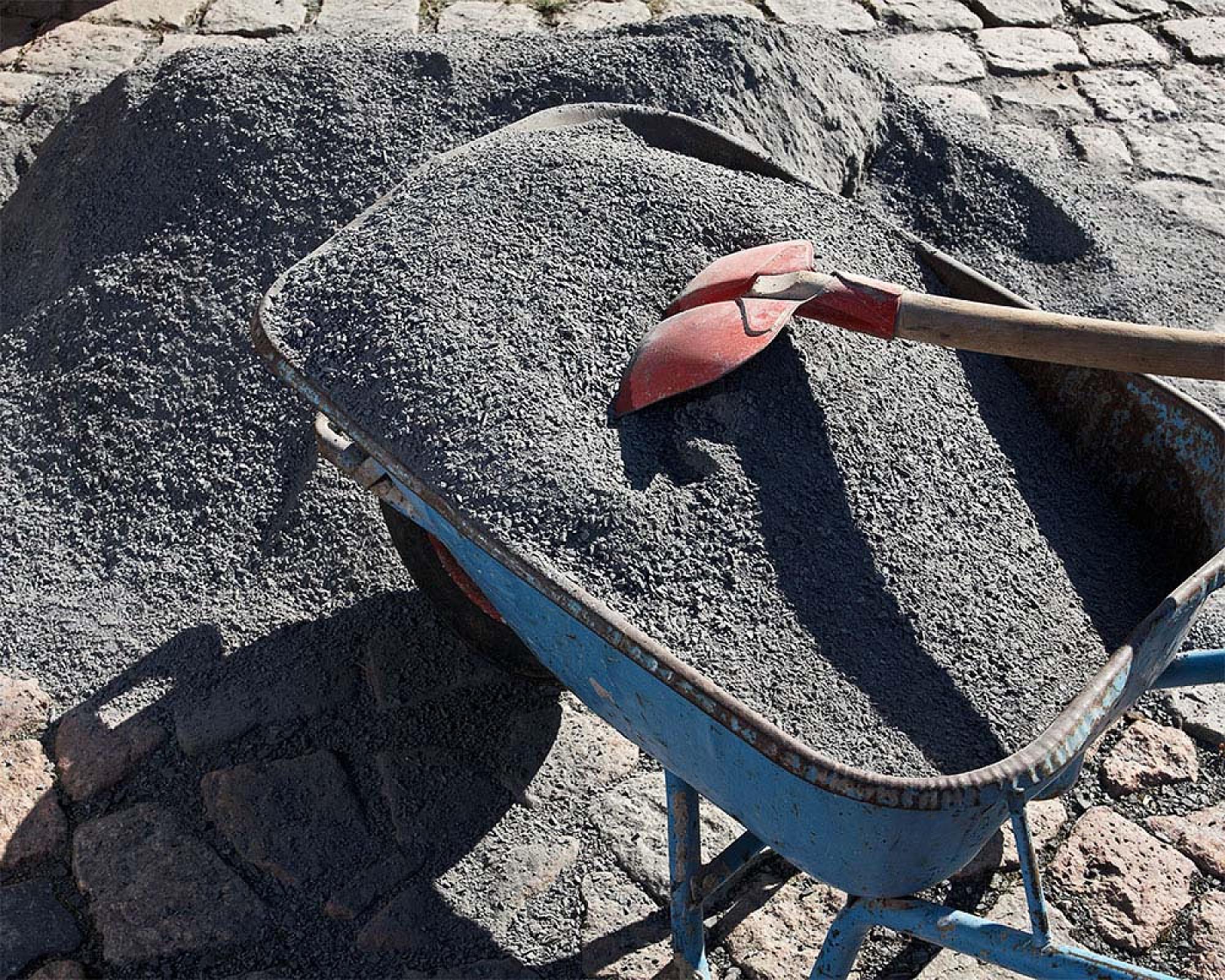 Schubkarre mit Basaltsplitt und roter Schaufel auf Kopfsteinpflaster.
