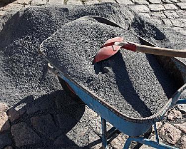 Schubkarre mit Basaltsplitt und roter Schaufel auf Kopfsteinpflaster.