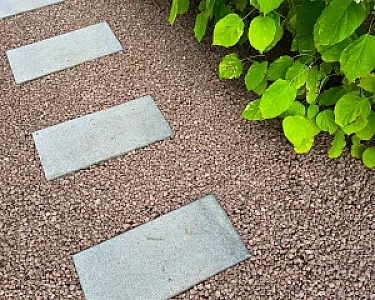 Gartenweg mit rotbraunem Lavakies und grünen Blättern.