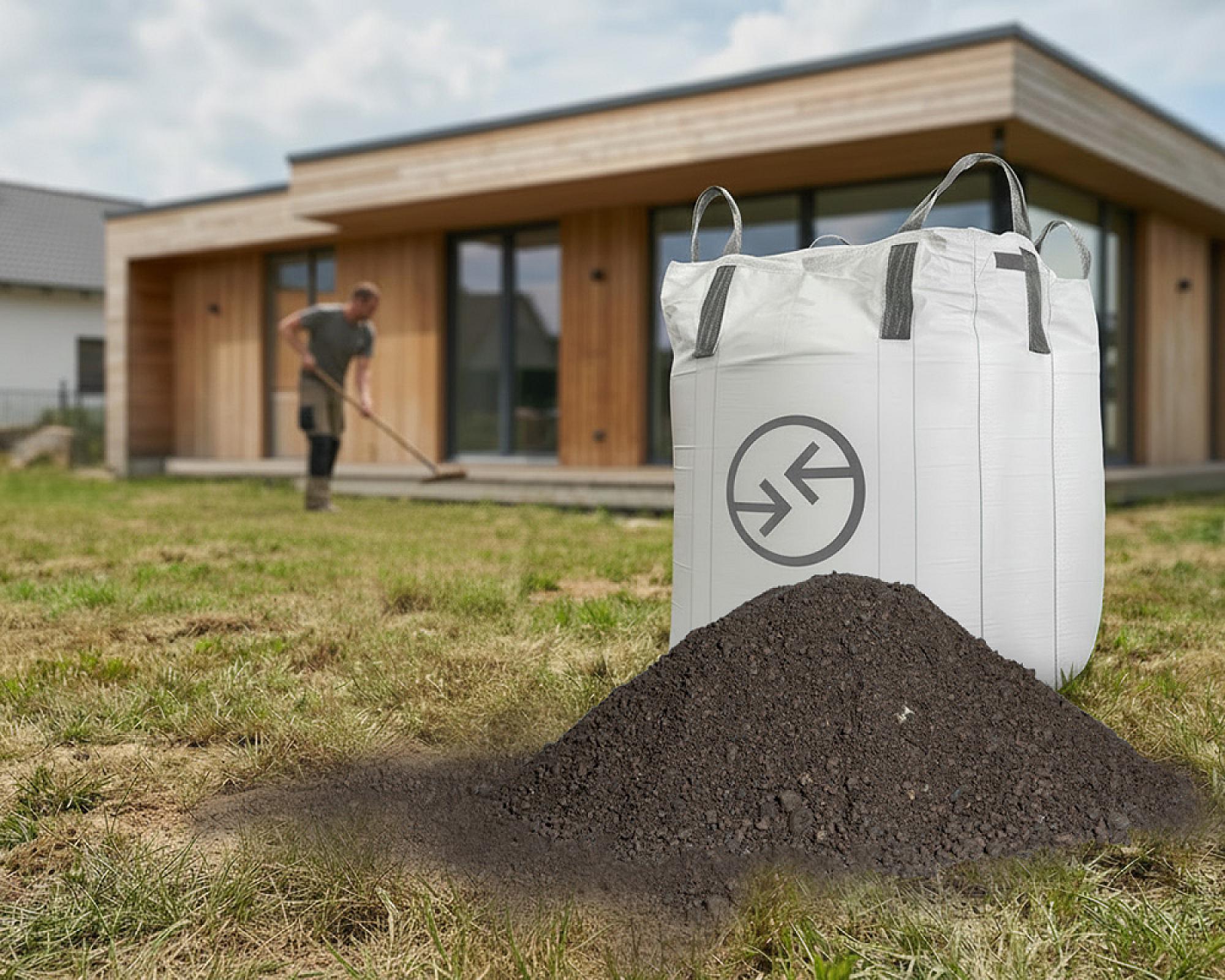 Bigbag mit Hellerwald Rasenerde vor modernem Holzhaus, im Hintergrund Person bei Gartenarbeit.