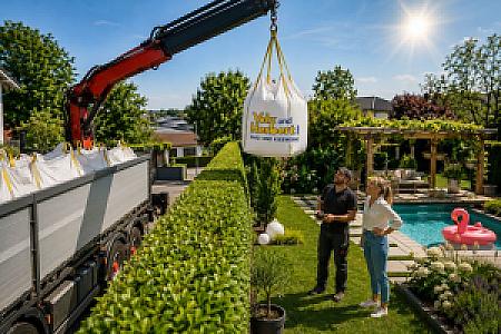 Kran hebt BigBag mit Volz und Herbert Aufschrift in einen Garten mit Pool.