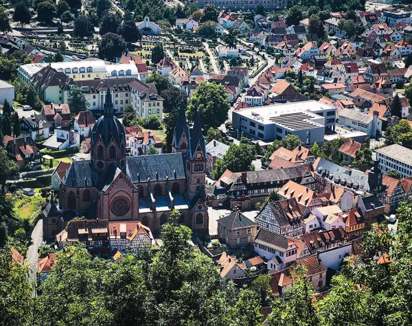 Ansicht einer malerischen Stadt mit historischen Gebäuden und einer großen Kirche in einer bergigen Landschaft.