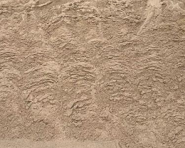 Beige Sandoberfläche mit wellenförmigen Mustern, möglicherweise von einer Sandwäsche oder natürlichen Erosion geformt.