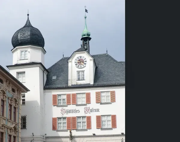 Historisches Gebäude mit Zwiebelturm und Uhr in der Stadt Rosenheim bei bewölktem Himmel.