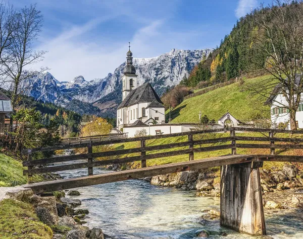 Eine malerische Kirche im Berchtesgadener Land vor schneebedeckten Alpen und einem klaren Bach.