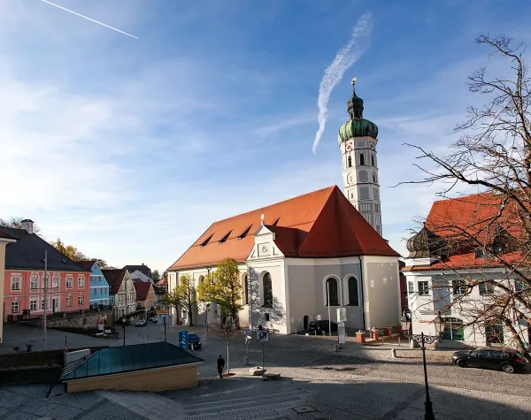 Stadtansicht von Dachau mit Kirche, bunten Gebäuden und blauem Himmel im Hintergrund.