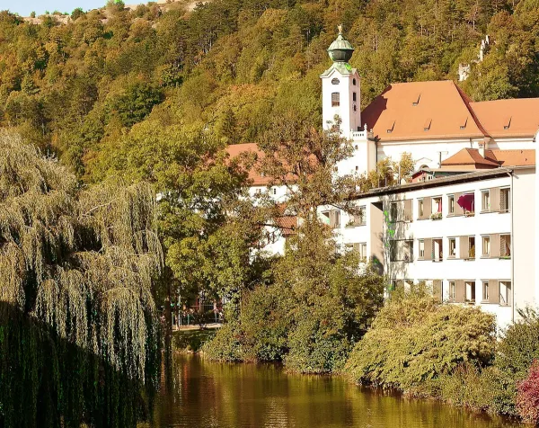 Historische Gebäude am Fluss in Eichstätt, umgeben von herbstlich gefärbten Bäumen.