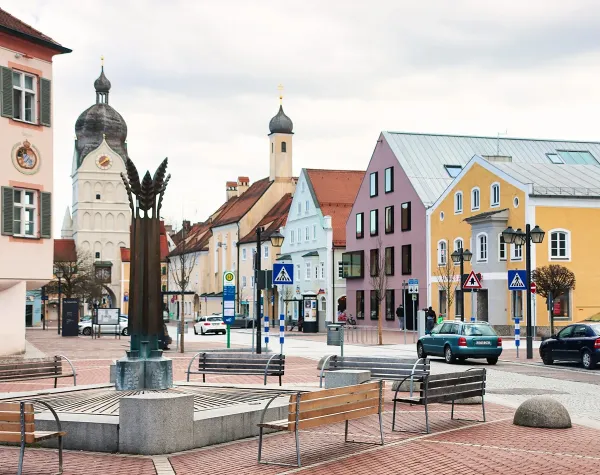 Historischer Marktplatz in Erding mit bunten Gebäuden und Kirche, umgeben von Sitzbänken und Fußgängerbereichen.