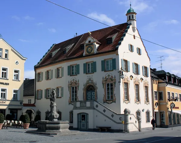 Historisches Gebäude mit verziertem Giebel und Uhr in Fürstenfeldbruck, Statue auf Brunnen im Vordergrund.