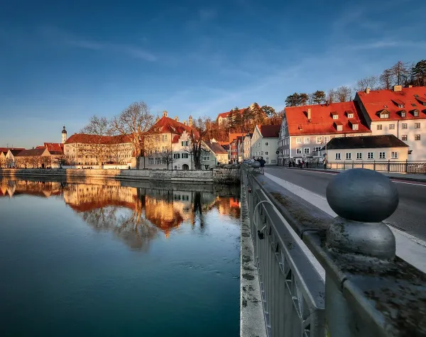 Idyllische Stadtansicht von Landsberg am Lech mit Fluss, Brücke und historischen Gebäuden bei klarem Himmel.