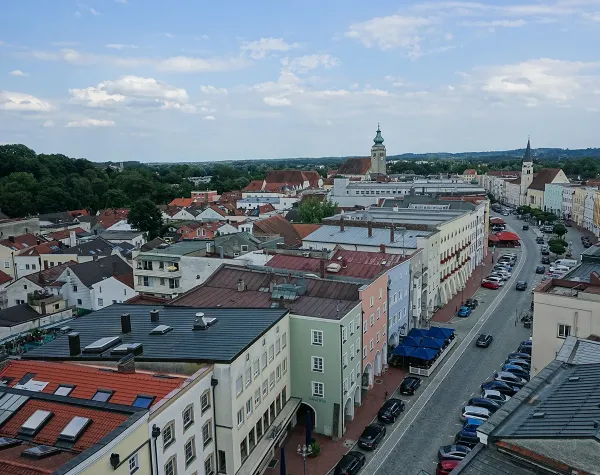Stadtansicht von Mühldorf am Inn mit pastellfarbenen Gebäuden und Kirchturm im Hintergrund.