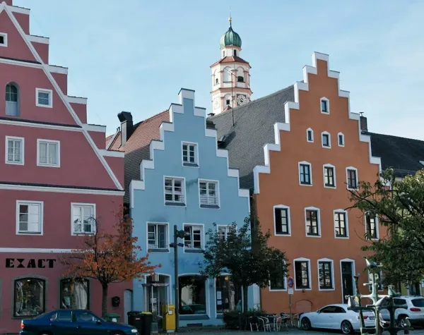 Bunte Giebelhäuser in Neuburg-Schrobenhausen mit Kirchturm im Hintergrund, blauer Himmel.