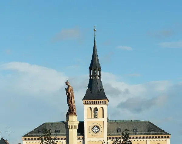 Kirchturm mit Uhr und Statue vor blauem Himmel in Pfaffenhofen an der Ilm.
