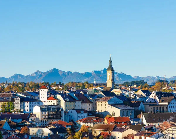 Stadtansicht von Traunstein mit Kirchturm im Vordergrund und Alpen im Hintergrund bei klarem Himmel.