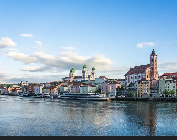 Panorama von Passau mit Dom und Altstadt entlang der Donau unter blauem Himmel.