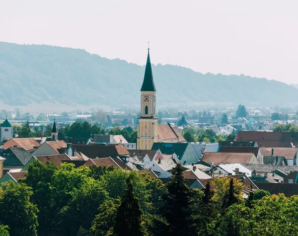 Stadtansicht von Kelheim mit Kirchturm im Vordergrund, umgeben von Hügeln und Bäumen.