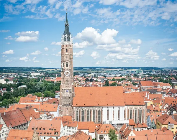 Stadtansicht von Landshut mit der St. Martinskirche im Zentrum vor einer Kulisse aus roten Dächern und blauem Himmel.