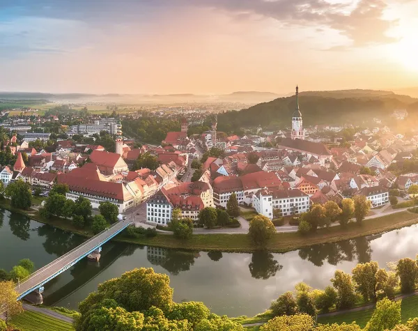 Panorama der Stadt Dingolfing-Landau mit Fluss, Brücke und historischen Gebäuden, umgeben von grüner Landschaft bei Sonnen...