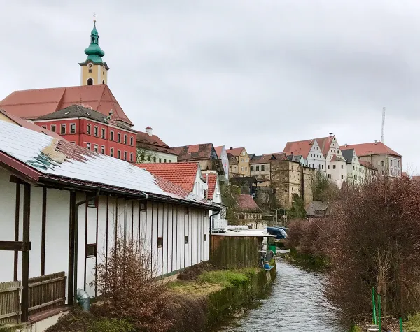 Historisches Stadtpanorama von Neustadt an der Waldnaab mit Fluss im Vordergrund und bunten Häusern im Hintergrund.