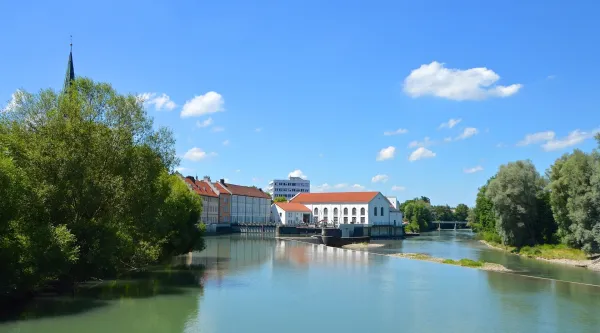 Fluss in Kempten mit Uferbäumen, historischen Gebäuden und blauem Himmel.