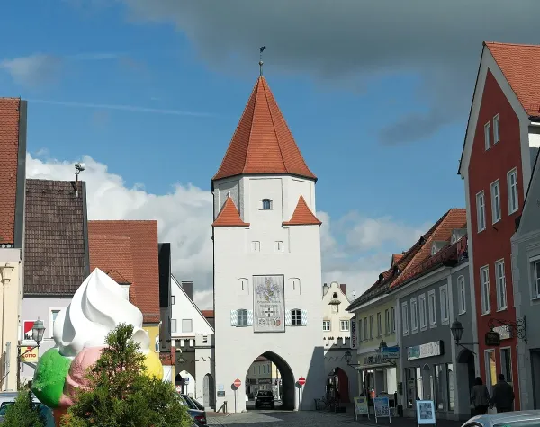 Historisches Stadttor in Aichach-Friedberg mit roten Dächern, umgeben von bunten Gebäuden und blauem Himmel.