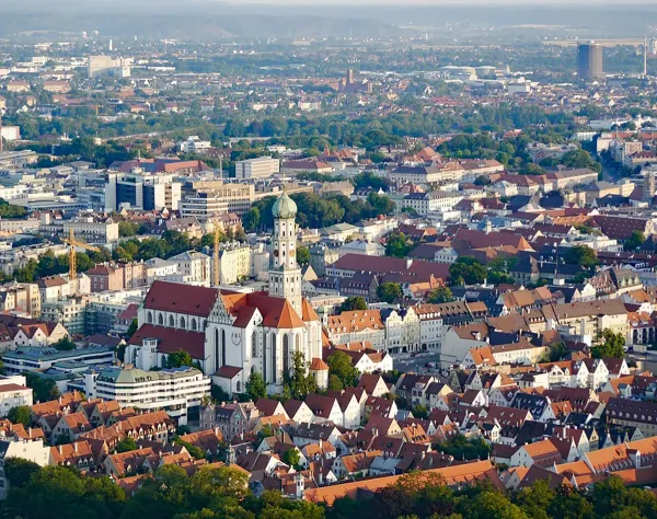 Augsburger Innenstadt aus der Vogelperspektive, mit historischen Gebäuden und der markanten Kirche in der Mitte.