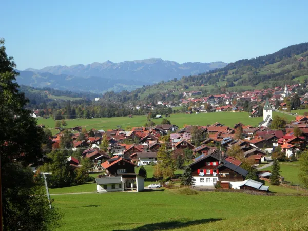 Idyllische Landschaft im Oberallgäu mit grünen Hügeln, verstreuten Häusern und Bergen im Hintergrund.