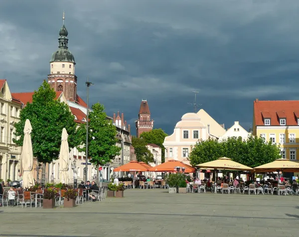 Marktplatz in Cottbus mit historischen Gebäuden, Kirchturm und Cafés unter wolkenverhangenem Himmel.