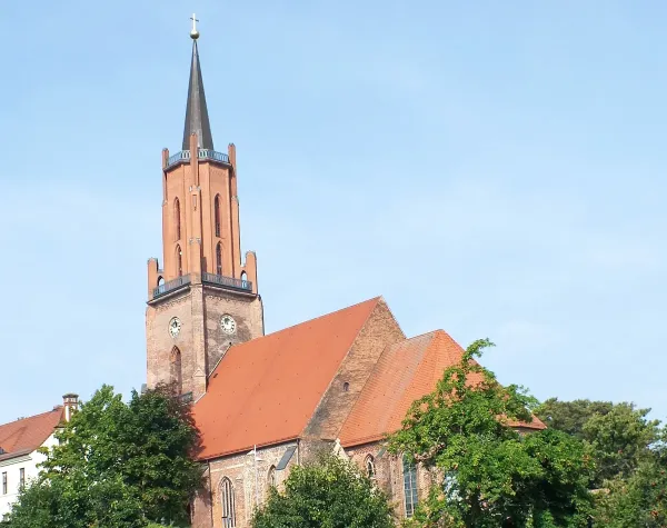 Kirche im Havelland mit rotem Ziegeldach und hohem Turm vor klarem Himmel.