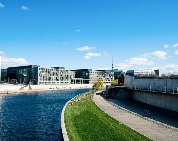 Moderner Bürokomplex am Ufer der Spree, mit breitem Gehweg und klar blauem Himmel.