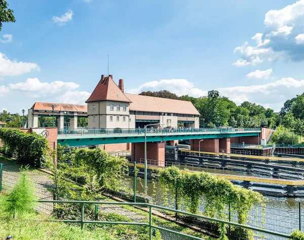 Historische Brücke mit rotem Dach über einem Kanal in Teltow-Fläming, umgeben von grüner Landschaft und blauem Himmel.