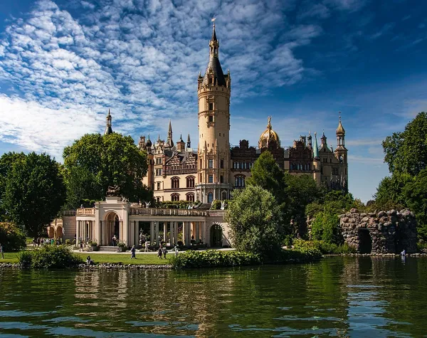 Historisches Schloss am Seeufer umgeben von üppigen Gärten und blauem Himmel in der Mecklenburgischen Seenplatte.
