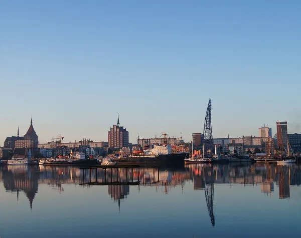 Panorama der Hafenstadt Rostock mit traditionellen Gebäuden und modernem Kran vor klarem, blauem Himmel.