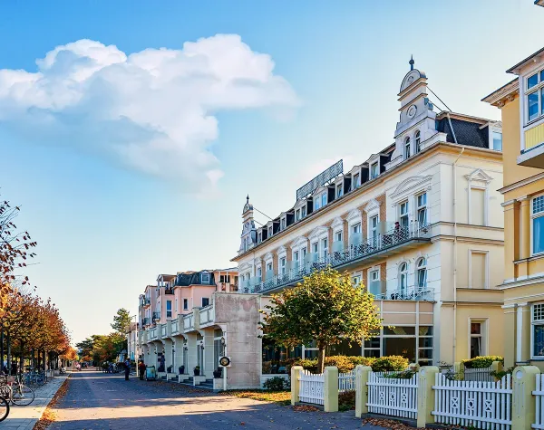 Häuserfassaden und herbstliche Allee in einem lebhaften Stadtteil von Landkreis Vorpommern-Rügen bei blauem Himmel.