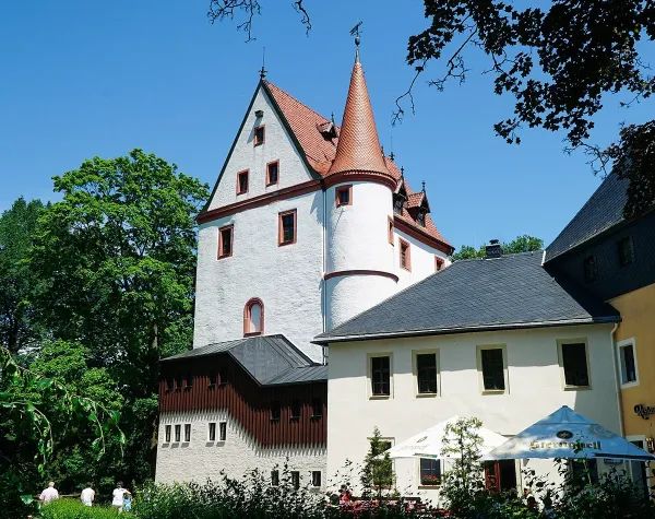 Weißer Burgturm mit orangem Dach im Erzgebirgskreis umgeben von Bäumen im Sommer.