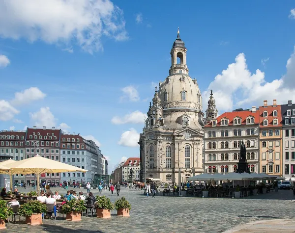 Die Frauenkirche in Dresden mit umliegenden historischen Gebäuden und Menschen auf einem belebten Platz bei klarem Himmel.