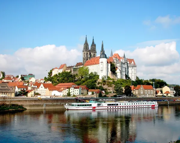 Stadt Meißen mit Albrechtsburg, Dom und Elbe im Vordergrund unter blauem Himmel.