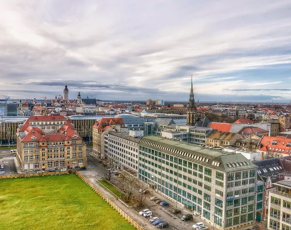 Stadtansicht von Leipzig mit historischen Gebäuden, Kirchturm und bewölktem Himmel.