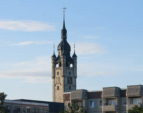 Kirchturm in Dessau-Roßlau vor blauem Himmel, umgeben von modernen Gebäuden.