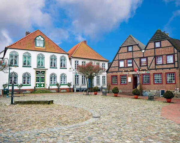 Historische Fachwerkhäuser auf gepflastertem Marktplatz in Dithmarschen unter blauem Himmel.