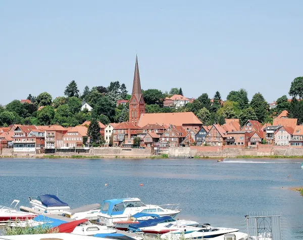 Herzogtum Lauenburg: Malerische Altstadt am Fluss mit Kirche, Booten im Vordergrund und bewaldeter Landschaft im Hintergrund.